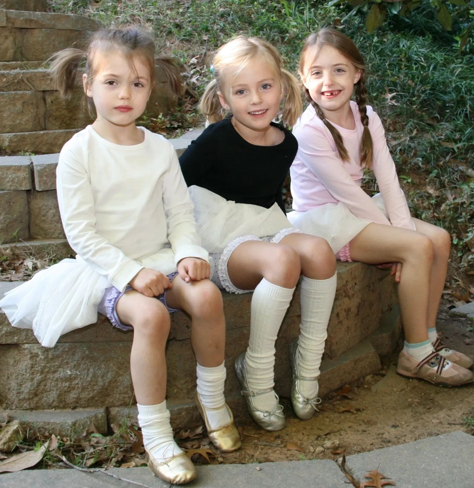 Three young girls in ballet attire sitting together outdoors